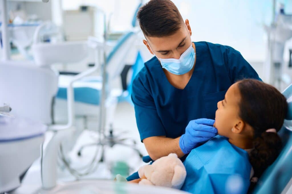 Young stomatologist checking teeth of girl in dentist’s office, applying dental sealants