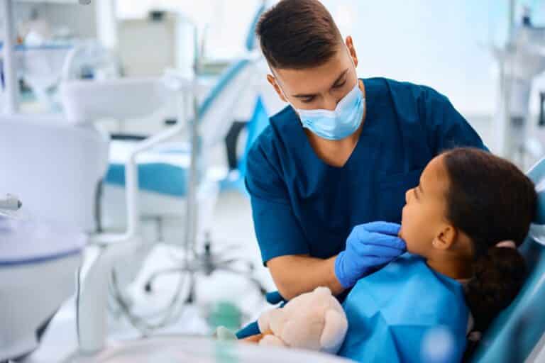 Young stomatologist checking teeth of girl in dentist’s office, applying dental sealants