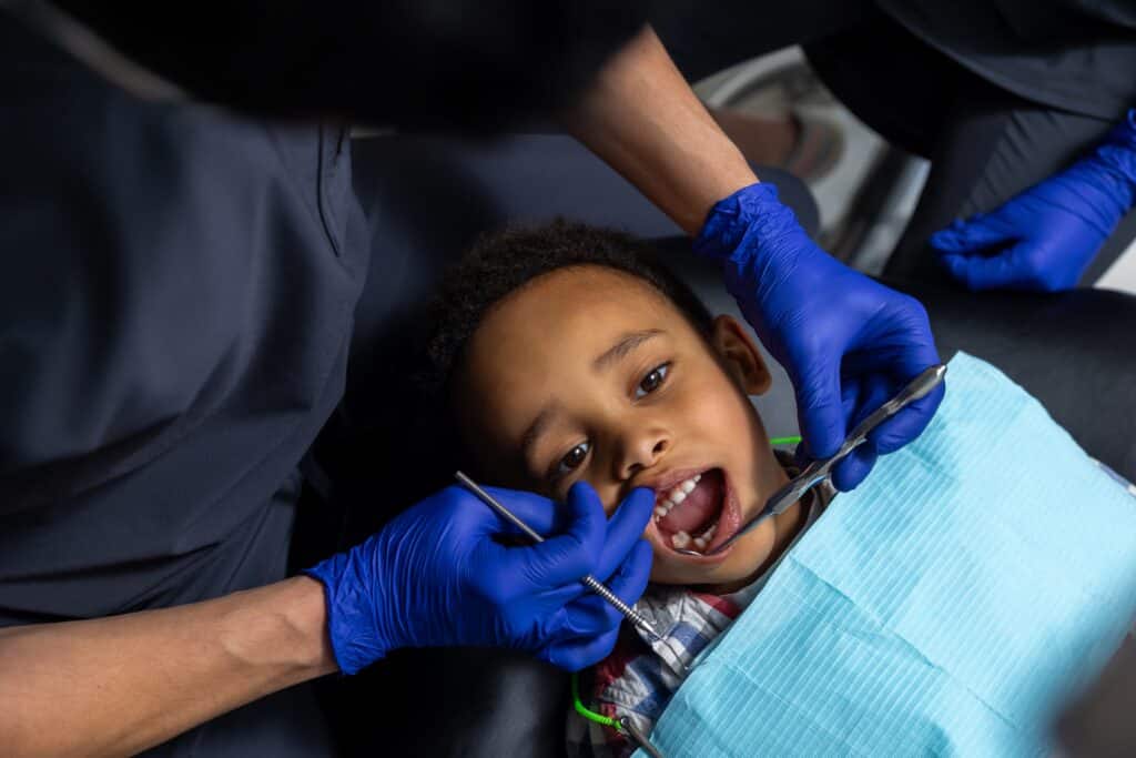 Dentist treating young boy’s teeth with dental fillings during oral care appointment