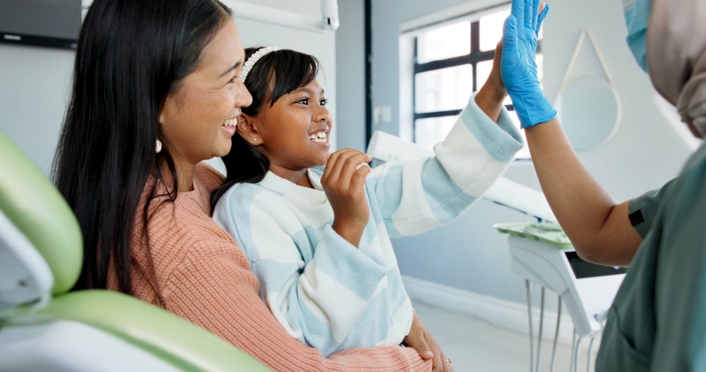 Pediatric dentist giving child a high five during dental checkup, showing trust, encouragement, and good oral hygiene habits.